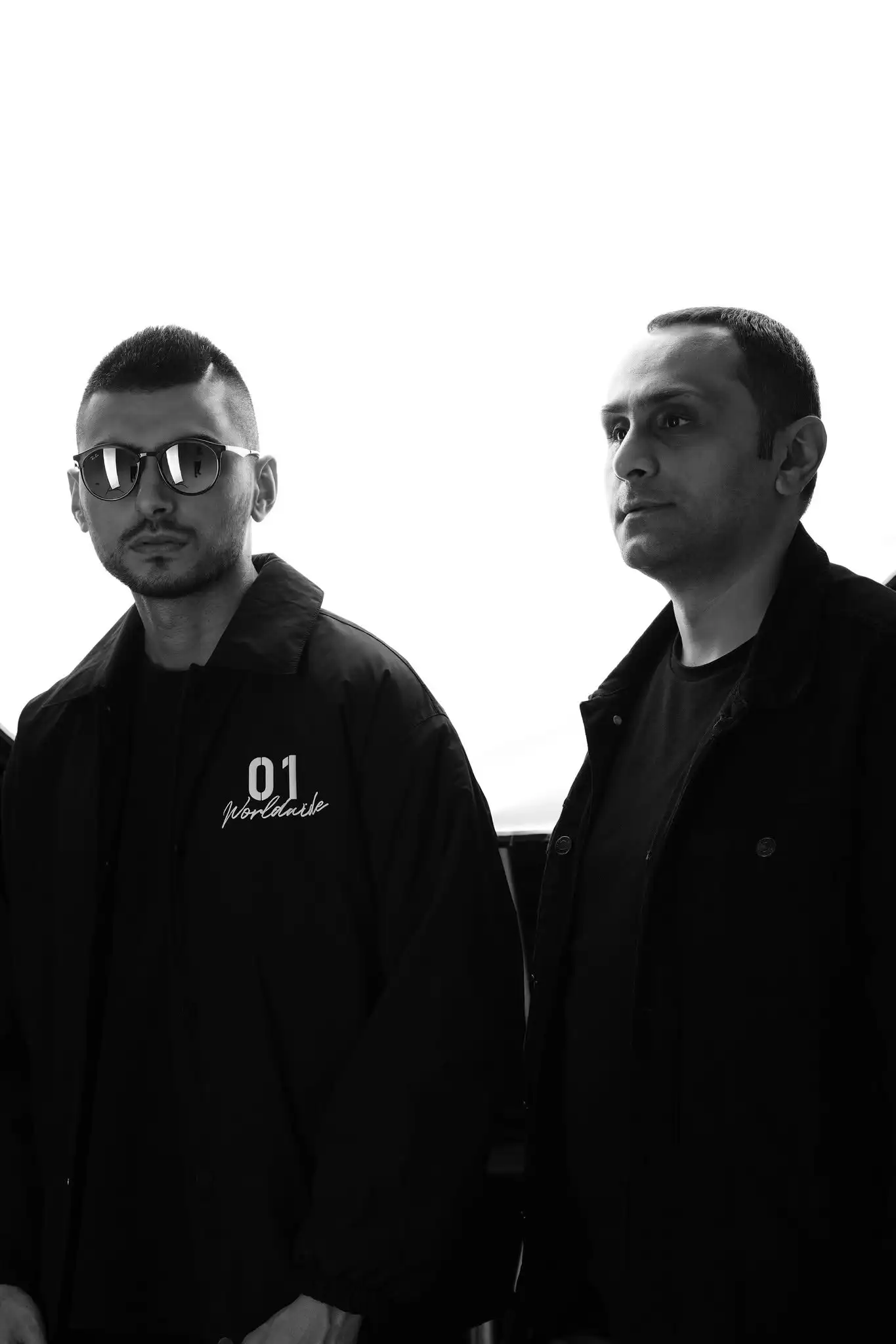 BakuBoy & Austin Blake in black jackets against a bright sky, in a black-and-white photograph.