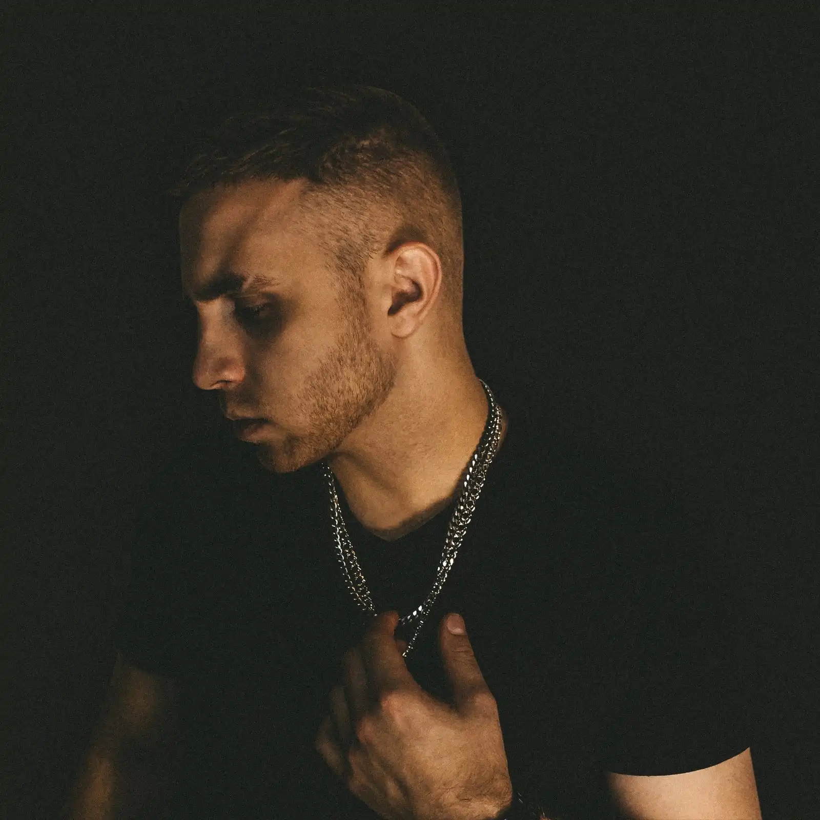 nesudi in profile against a dark background, wearing a silver chain.